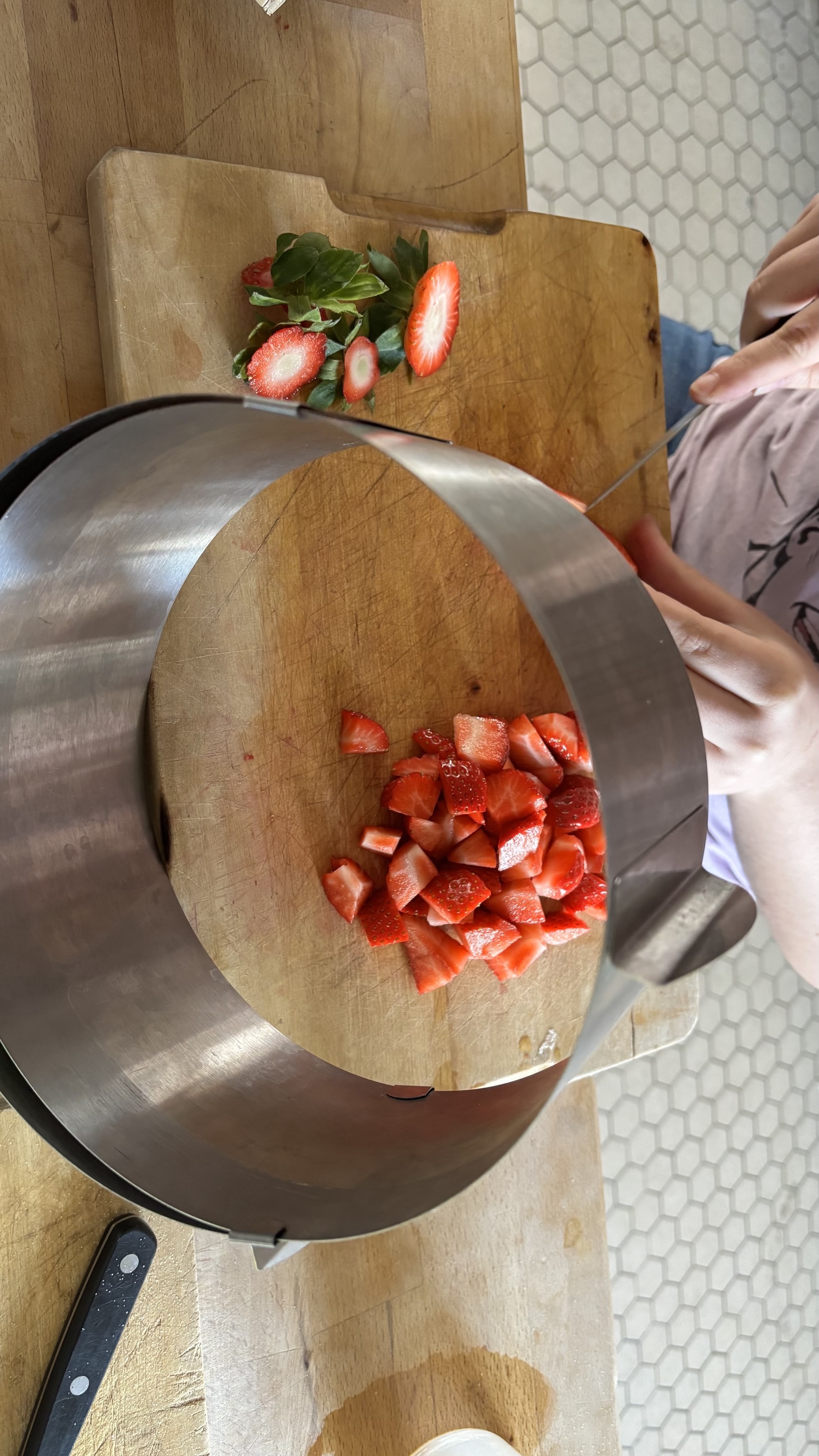 Une planche est posée sur une table, un cercle à gâteaux est posé en équilibre contre la planche sur laquelle trônent des fraises coupées et dés.