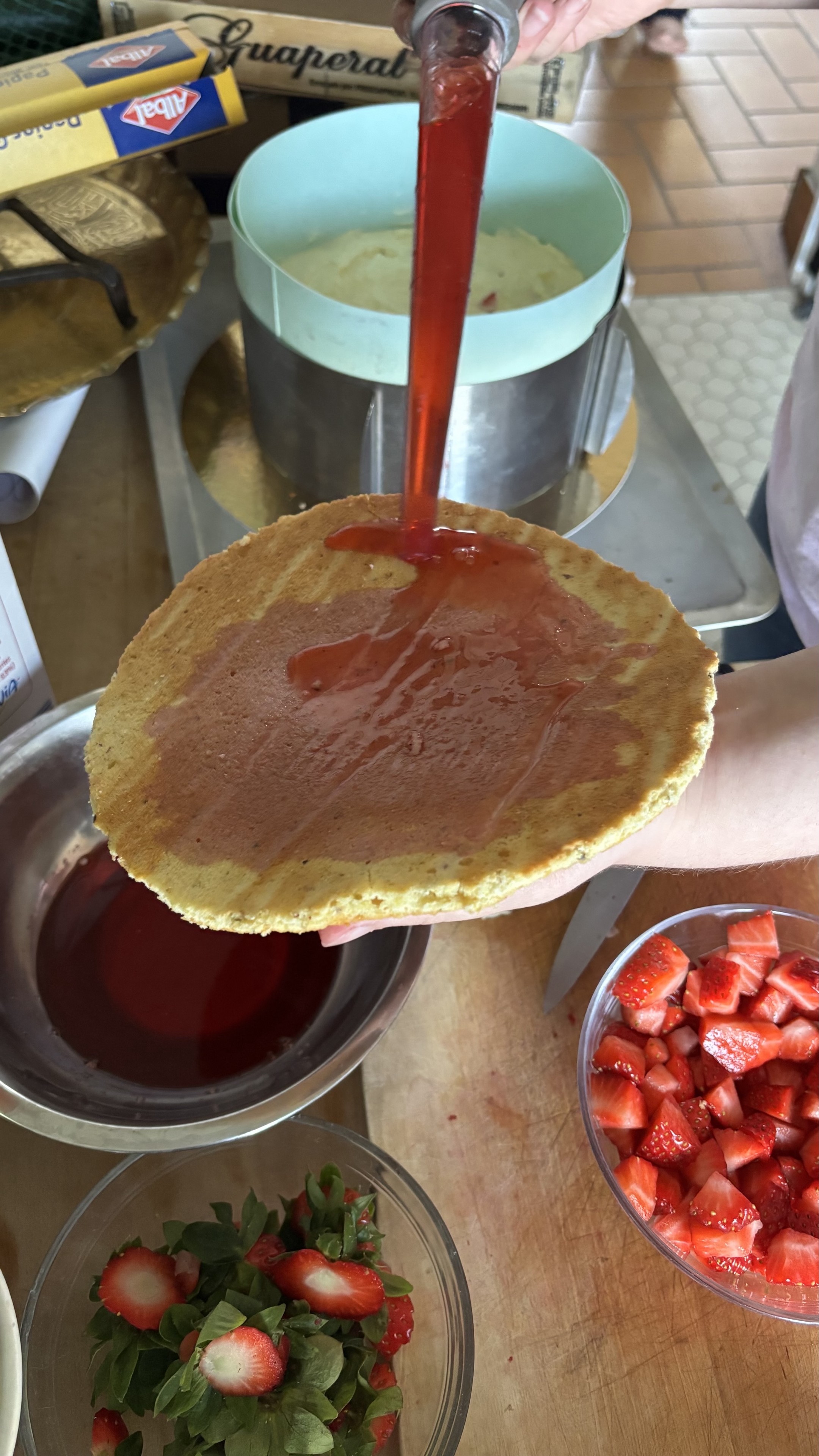 Levantine tient dans sa main un disque de gâteau qu’elle badigeonne de jus de fraise fraîchement extrait à l’aide d’une poire.