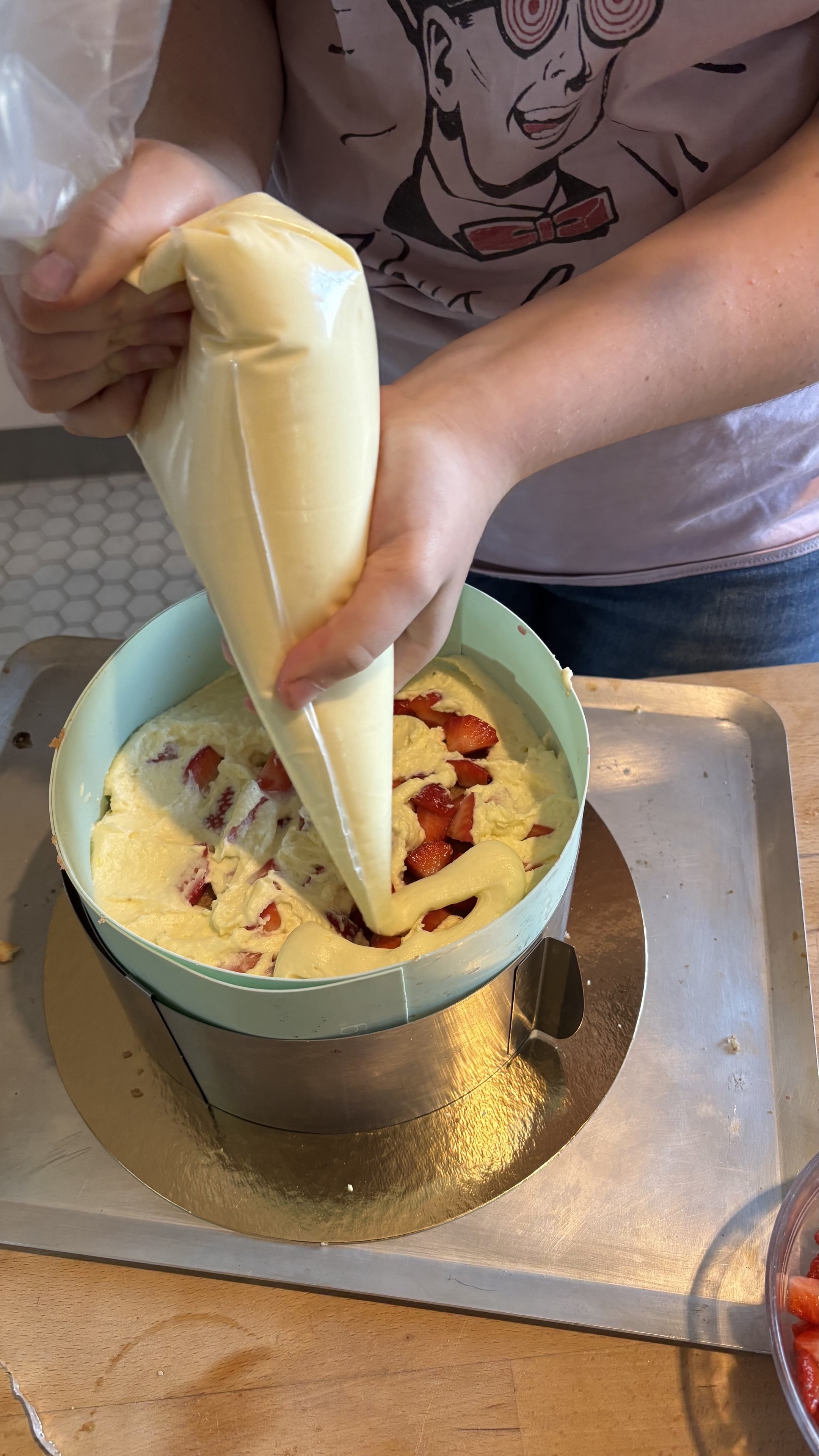 A l’aide d’une poche à douille Levantine couvre des fraises dans son fraisier avec une crème pâtissière montée.