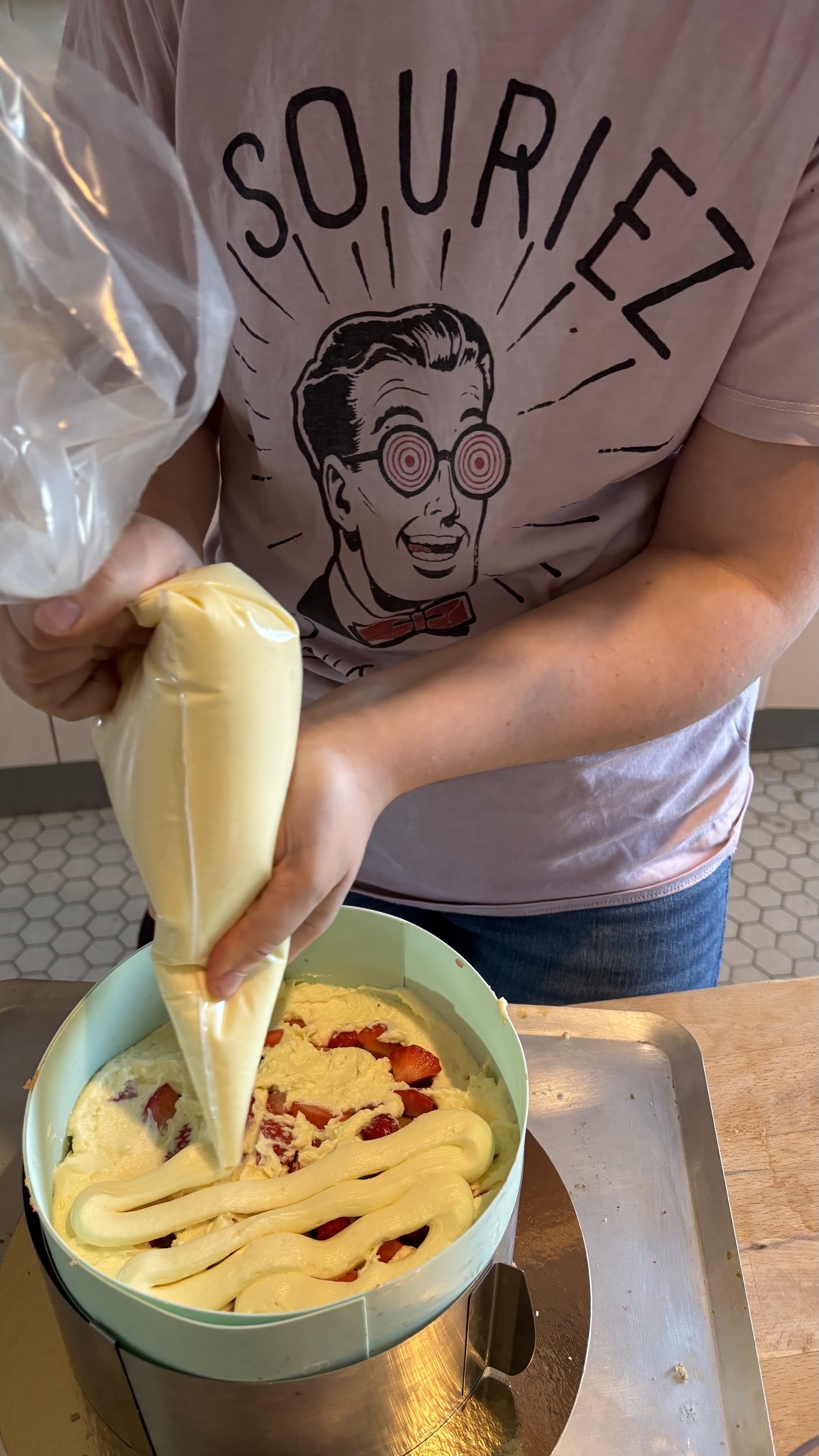 A l’aide d’une poche à douille Levantine couvre des fraises dans son fraisier avec une crème pâtissière montée.