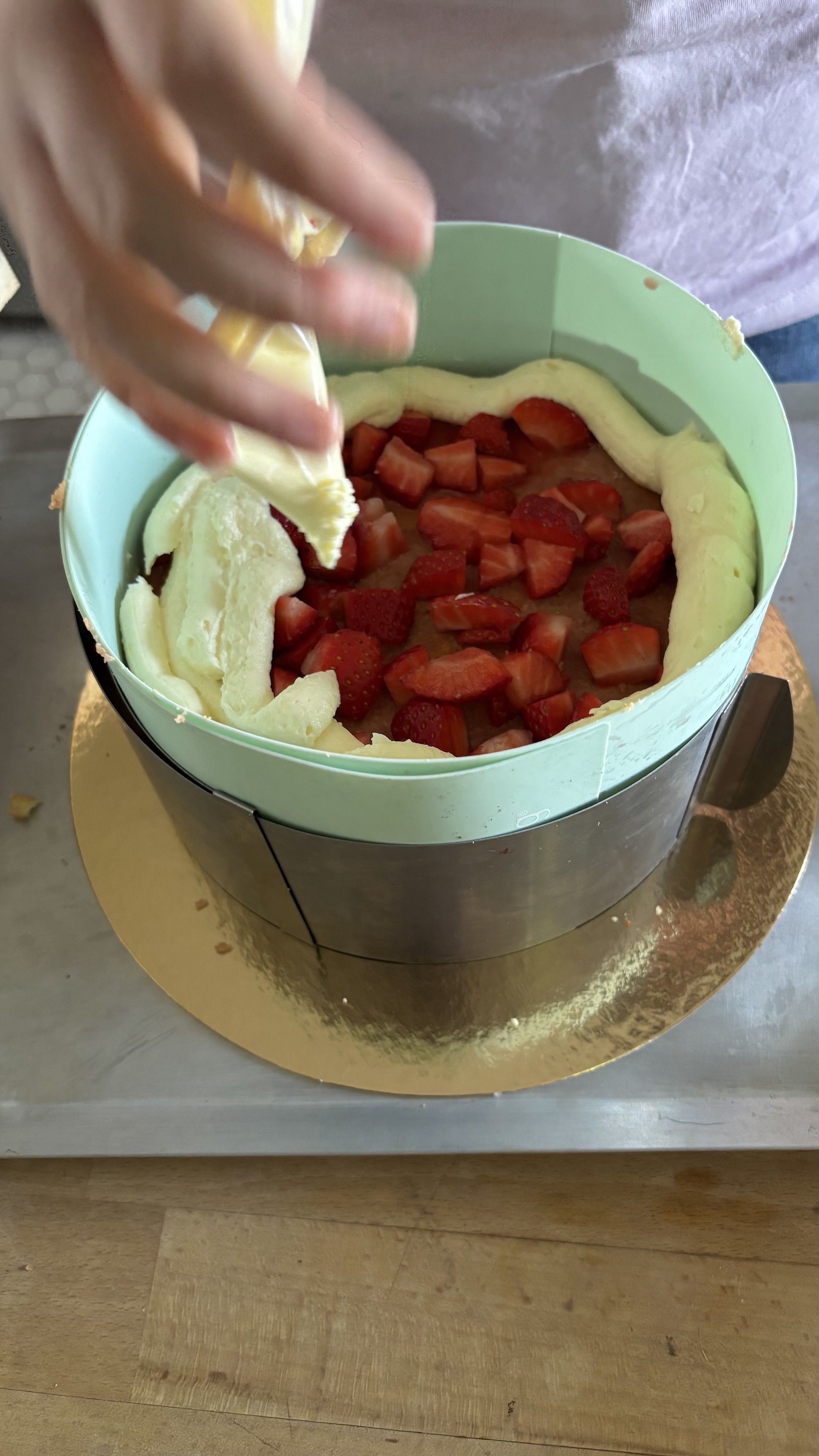 A l’aide d’une poche à douille Levantine couvre des fraises dans son fraisier avec une crème pâtissière montée. Mais la on voit des fraises car le fraisier en est plein.